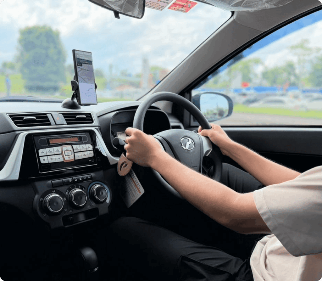 Driver’s hands on steering wheel inside a car with dashboard and mounted navigation phone.